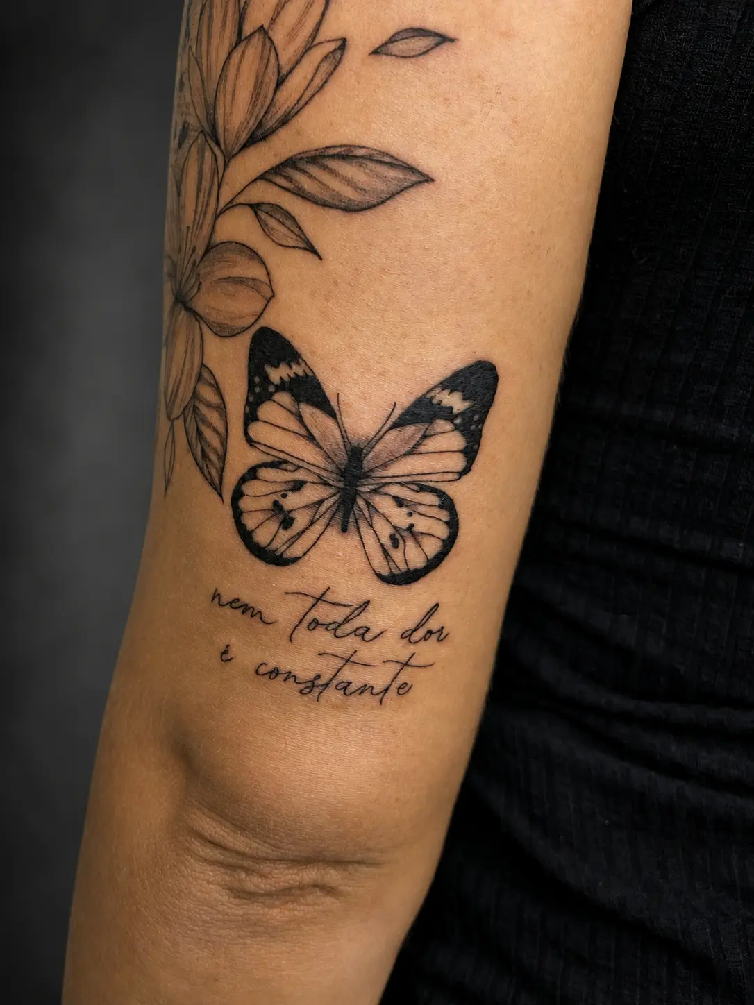 Tatuagem de borboleta e flores com frase no braço
